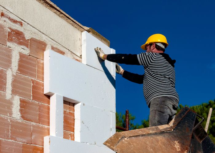 un artisan isole thermiquement l'exterieur de la maison